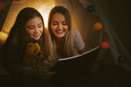 mother reading a book to her daughter indoors before going to bedの写真素材