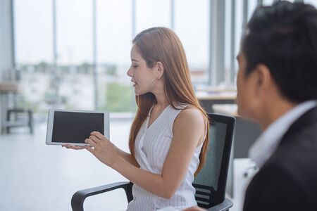 Asian Woman showing discussing present by tablet to colleaguesの写真素材