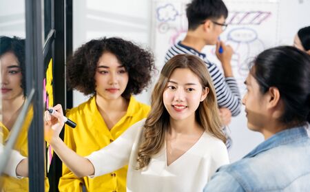 Group of Asian business people meeting at modern office. Young creative team use   notes to share idea sticky note on glass wall. and working design planning and Brainstorming concept.の写真素材