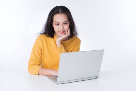 Young Asian woman working on laptop she wearing a yellow sweater shot isolated on white backgroundの写真素材