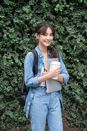 Portrait of young Asian woman student standing with laptop coffee and backpack.College Teenager...