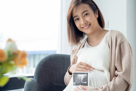 Asian pregnant woman showing ultrasound picture at home