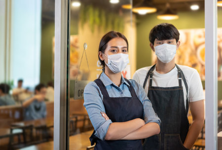 Portrait of Young couple restaurant owner wearing protective mask stand in in front of restaurant .の写真素材
