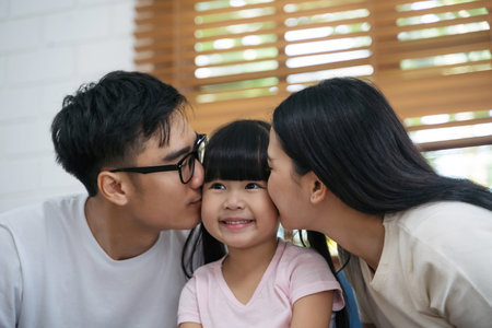 Happy young asian father and mother are kissing her daughter's cheek. Happy family enjoy spending a good time together in a house. Happy asian family.の写真素材