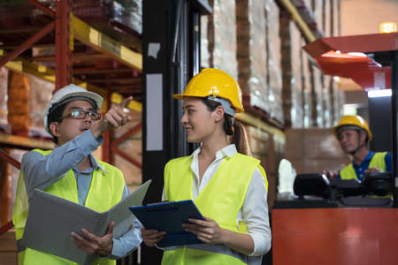 Asian factory manager and engineer woman working in warehouse. Warehouse worker talking about storage department controlling logistic distribution to the market.の写真素材