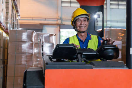 Portrait of happy Asian old man working in warehouse and sitting on forklift work with positive emotion.の写真素材