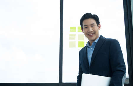 Portrait asian Asian businessman smiling confidently while standing in office with holding laptop.の写真素材