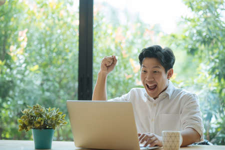 Asian man celebrating success while working on laptop at home.の写真素材