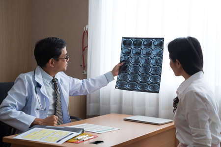 Asian doctor holding x-ray radiography to patient reviewing brain X-ray.