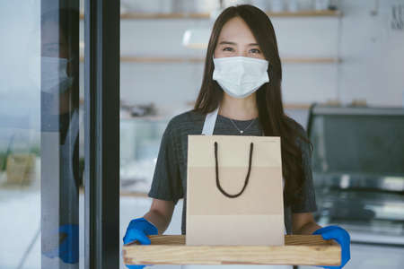 Asian waitress with face protective mask delivering takeaway coffee and food bags to customersの写真素材