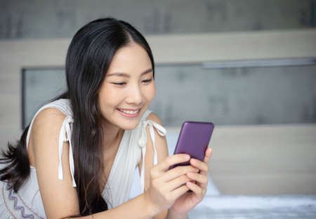 Young Asian woman using smart phone in bedroom happy and smile.の写真素材