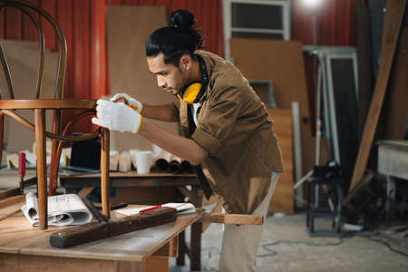 Young Asian man Carpenter uses a tape measure to measure chair on the workbench in woodcraft carpentry workshop.の写真素材