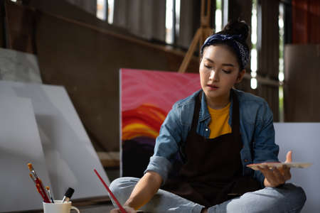 Asian Female Artist Draws create art piece with palette and brush painting at studio.の写真素材
