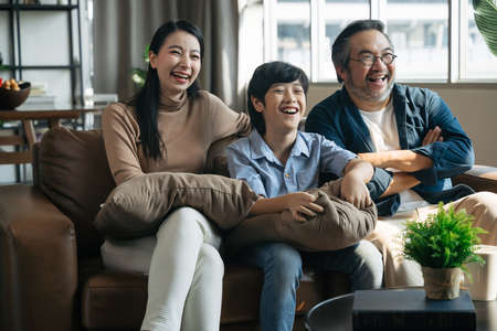Happy Asian family spending time by watching tv together on sofa in living room. family and home conceptの写真素材
