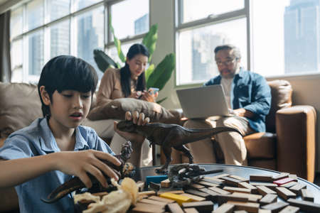 Son play with rubber dinosaur figures and while parents working at sofa in living room. family and home concept.の写真素材