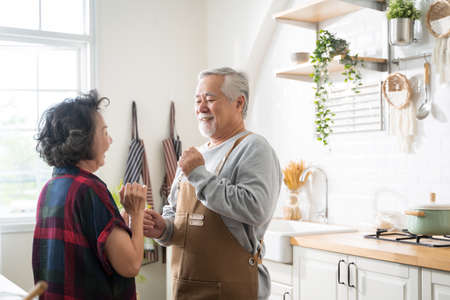 Asian mature senior couple is dancing and smiling in kitchen at home.の写真素材