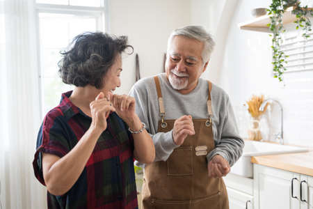 Asian mature senior couple is dancing and smiling in kitchen at home.の写真素材