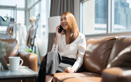 Asian woman on the phone talking on the sofa happily and smiling.の写真素材