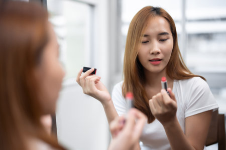 Asian woman looks lovely Female Applying Lip Balm Moisturizing Caring For Skin While Standing Near Mirror routine makeup at home.の写真素材