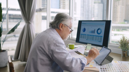 Asian senior mature man working with computers and tablet on table desk at homeの写真素材