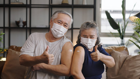 Asian mature couple show shoulder with band aid after injection and giving a thumbs up after being vaccinated.の写真素材
