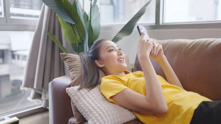 Asian woman on the phone talking on the sofa happily and smiling.の写真素材