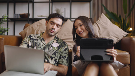 Young couple using tablet and laptop together on sofa in living room at homeの写真素材