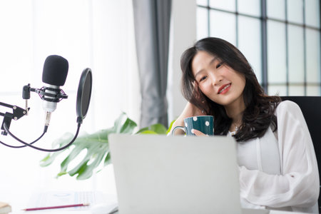 Asian woman working on laptop computer with headphones and microphone at home relaxing and chilling happily.の写真素材