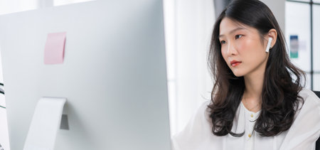 Young asian girl working at a home with a computer and wearing earphonesの写真素材