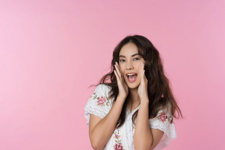 Young Asian woman doing a shocked surprise gesture shouting with hands cupped around mouth isolated...