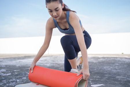 Young Asian woman picking up yoga mat after exercising.outdoor exercise fitness conceptの写真素材