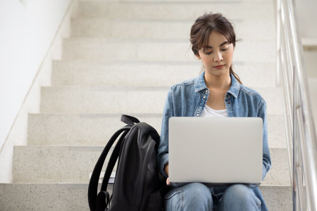 Asian student woman working on a laptop on stairs on university campus.