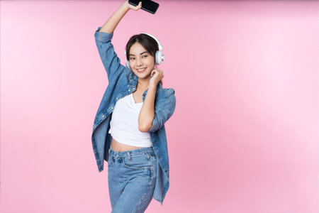 Young Asian woman wearing headphones dancing and listening to music from smartphone shoot in isolated on pink backgroundの写真素材