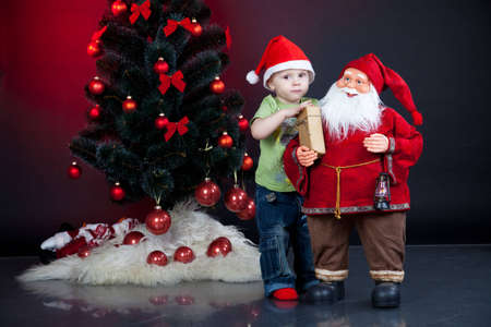 little baby boy with christmas tree and santa on red backgroundの写真素材