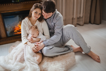 young happy family sitting on floor near fireplace in their apartmentの写真素材