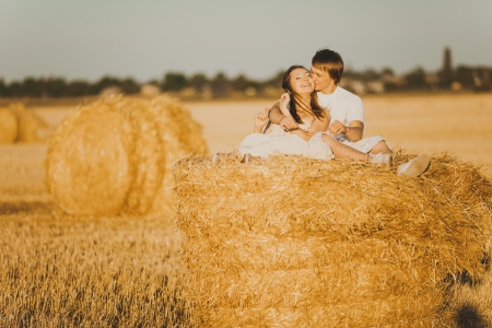 Image of young loving couple sitting on haystack in fieldの写真素材
