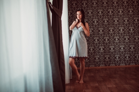 Pregnant woman put her hands her belly on standing at the windowの写真素材