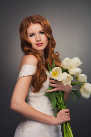 beautiful bride with curly red hair in wedding dress with flowersの写真素材