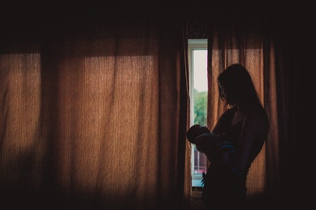 Young mother holding newborn baby near windowの写真素材