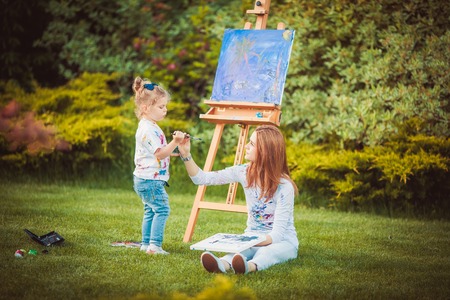 Mother and little daughter paint together in a parkの写真素材