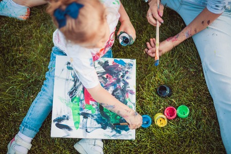 Mother and little daughter paint together outdoorsの写真素材