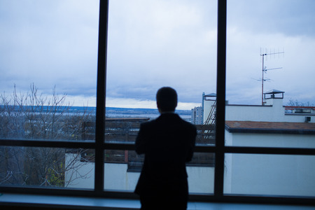 Businessman thinking in office, looking out of windows to downtownの写真素材