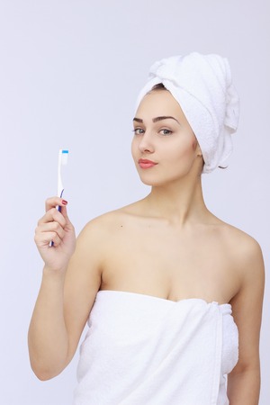 young beautiful woman wrapped in towel brushing her teeth isolated on white backgroundの写真素材