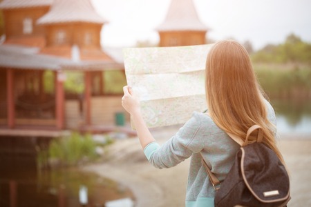 Back side of traveler girl searching right direction on map, orange sunset light, traveling along...