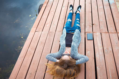 Young woman relaxing on pier. laying on the pier and watching in the sky. listening some musicの写真素材