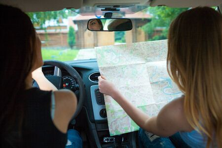 Two girls traveling in a car. Couple of girls spending weekend on nature. Searching road to go