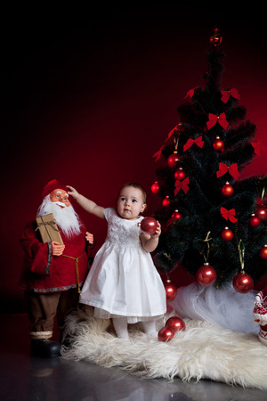 little baby girl with christmas tree and santa on red backgroundの写真素材
