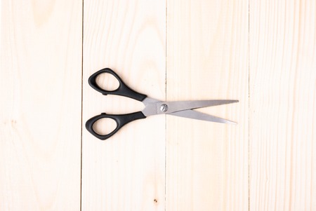 One black scissors isolated on wooden background