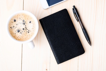 Smartphone with notebook and cup of strong coffee on wooden background