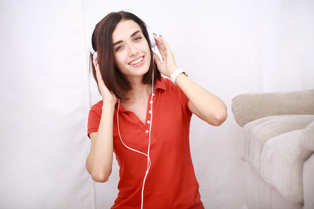Woman listening music in headphones sitting on sofa in room. Happy relaxing girl. Closeup portraitの写真素材